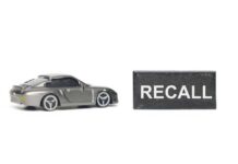 Recall Panic: Fuel Tanks Can Drop A miniature gray sports car next to a black sign that reads 'RECALL'