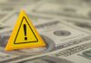 Gas Pump Gut-Punch Hits $100 Billion A yellow warning sign placed on a pile of dollar bills