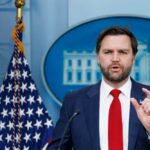 FEMA Whiplash: Fired Boss Returns Man in suit speaking at a podium with U.S. flag and emblem backdrop