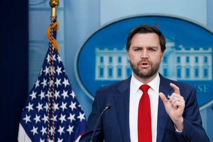 Man in suit speaking at a podium with U.S. flag and emblem backdrop