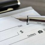 Paycheck Ambush Coming in 2027 Close-up of a fountain pen poised over a blank check
