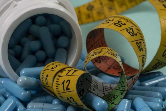 A,Close-up,Shot,Showing,Numerous,Blue,Capsules,Or,Pills,Spilling Blue capsules spilled from a white bottle alongside measuring tapes