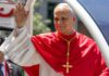 Catholic cleric in red vestments waves from a vehicle