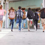 Pay Soars, Buses Still Empty – WHY? Children running with backpacks outside a school building.