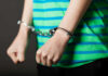 11-Year-Old Booked In Brother’s Killing Person in striped shirt wearing handcuffs.