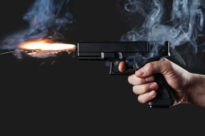 A hand holding a gun with smoke and a flash from the muzzle