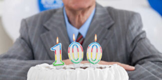Birthday cake with 100 candles, person in background.