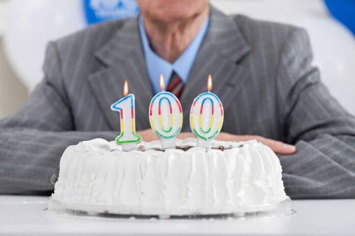 shutterstock_161175410 Birthday cake with 100 candles, person in background.