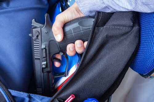 A hand holding a gun inside a backpack