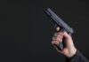 Gunfire Erupts Near White House Hand holding a black semi-automatic pistol against a dark background