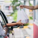 Drive-Thru Disrupted By Gas-Station Grub Customer receives a takeout bag at a drive-thru window