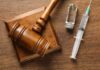 A wooden gavel next to a syringe and a vial on a wooden surface