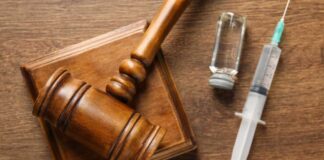 A wooden gavel next to a syringe and a vial on a wooden surface