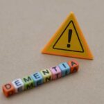 Raspy Voice Tied To Dementia? Colorful letter blocks spelling 'DEMENTIA' next to a warning sign