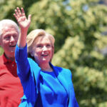 Clinton Drops Midterm Bombshell Hillary Clinton waving at an outdoor event with Bill Clinton in the background